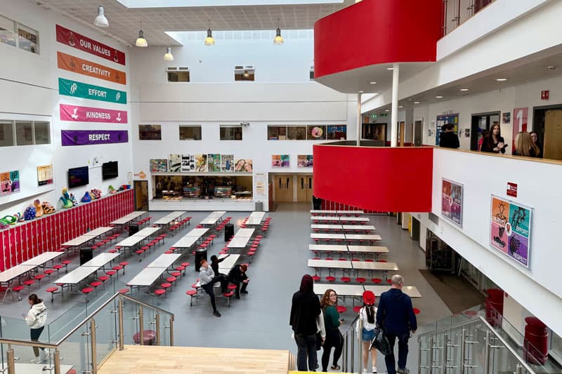 Helle Schulmensa mit roten Stühlen und Galerie über mehrere Etagen – College-Alltag in Großbritannien