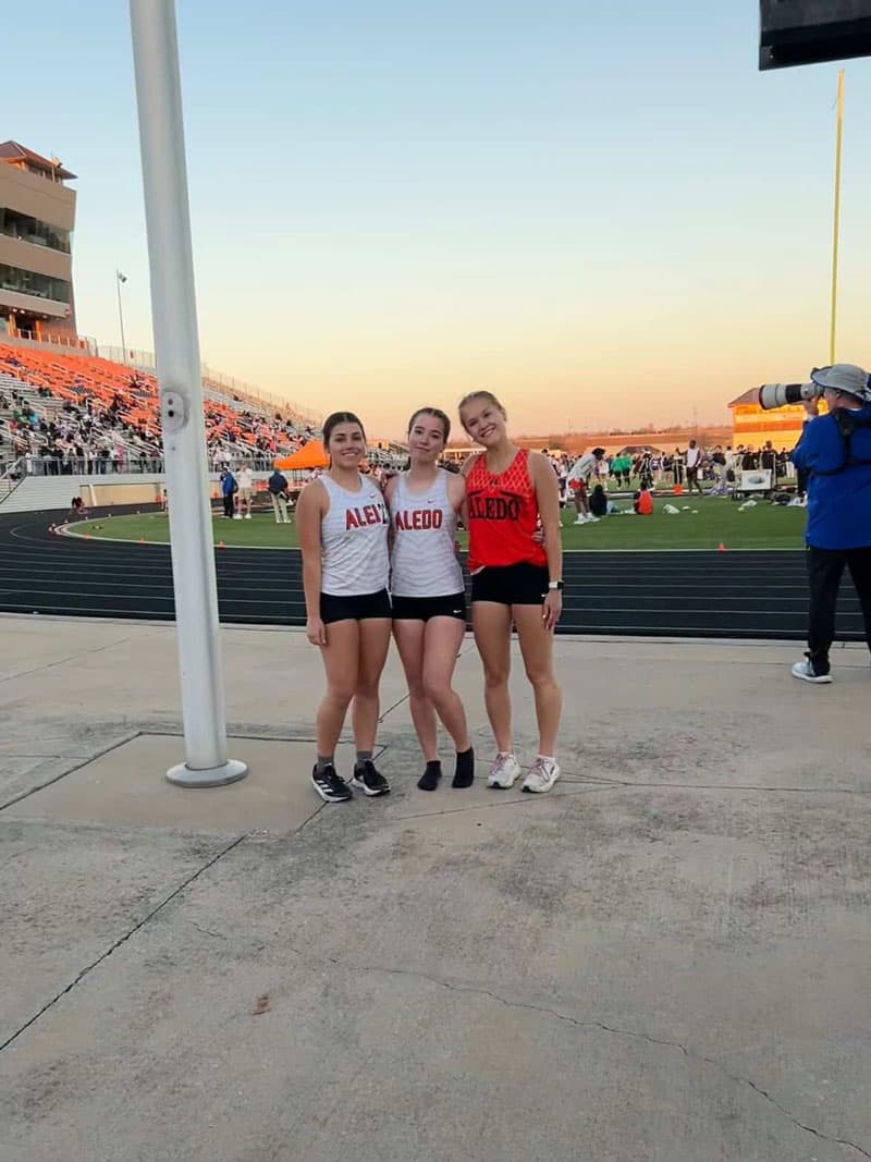 Leichtathletik an der High School: drei Athletinnen in Aledo-Trikots im Stadion bei Sonnenuntergang