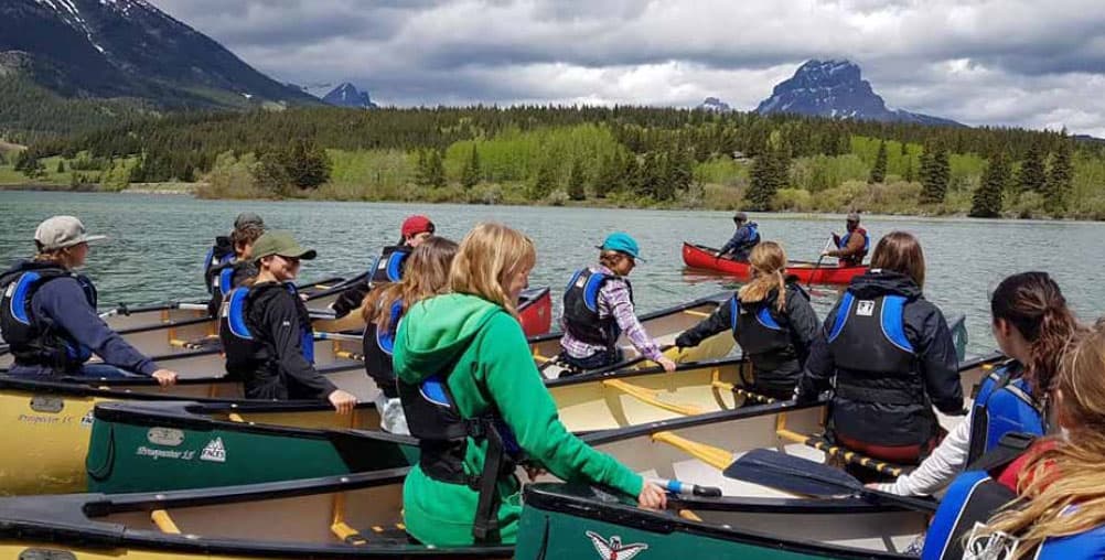 Austauschschüler:innen mit Schwimmwesten in Kanus auf einem Bergsee in Alberta
