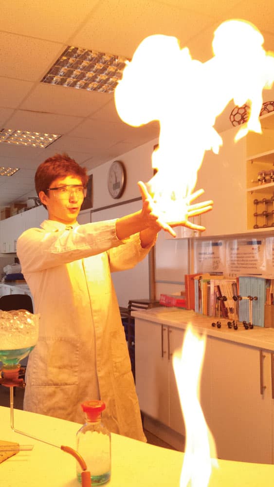 Chemieunterricht im Auslandsjahr in England: Schüler im Laborkittel zeigt ein Flammenexperiment