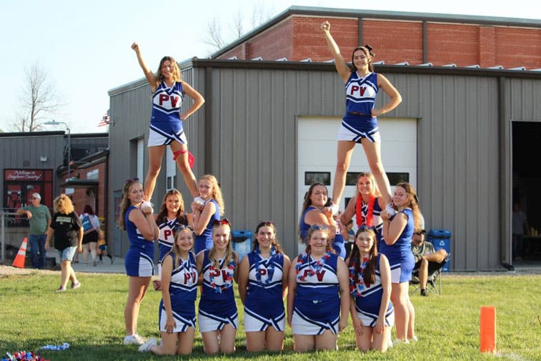 Cheerleaderinnen einer High School in blauen Uniformen bilden eine Pyramide auf dem Rasen