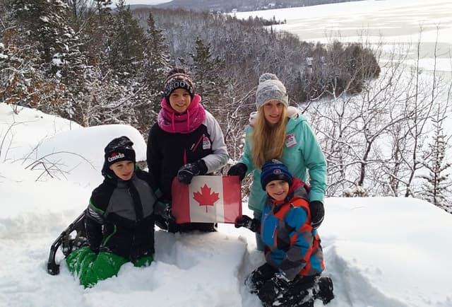 Gastfamilie mit Kindern und kanadischer Flagge im tiefen Schnee