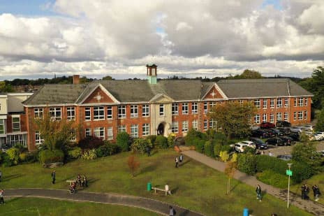 Großes Backsteingebäude einer englischen Schule mit Rasen und Wegen unter Wolken