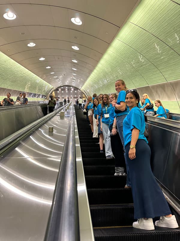 Schüleraustausch-Gruppe in blauen T-Shirts auf einer langen Rolltreppe in einer U-Bahn-Station