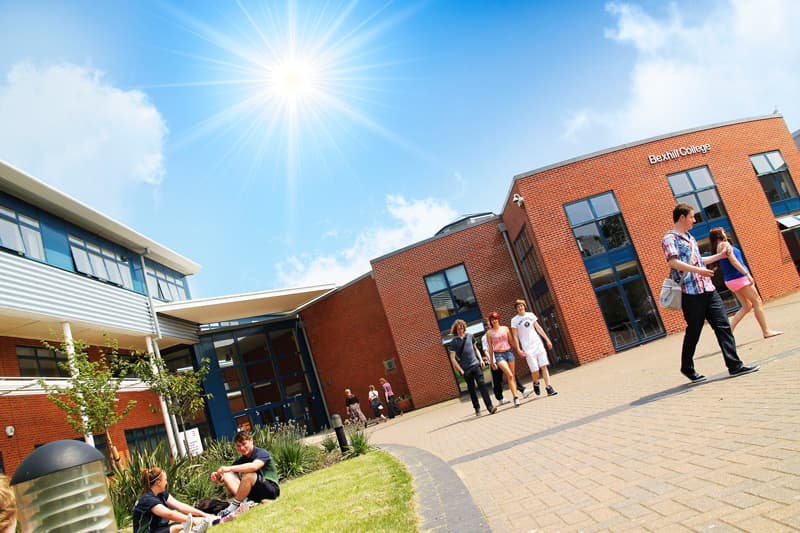 Moderne Backsteinschule mit Schüler:innen auf dem Vorplatz bei strahlender Sonne in Südostengland