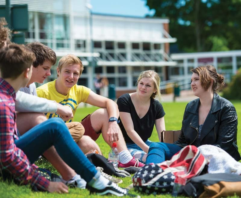 Pause im Auslandsjahr: Schüler:innen unterhalten sich im Gras vor einem Schulgebäude in England