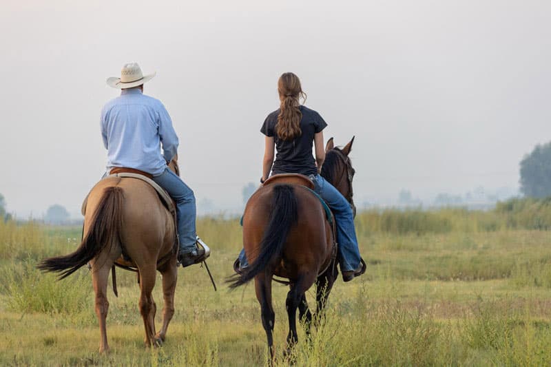 Gastvater mit Cowboyhut und Austauschschüler:innen reiten über eine Wiese im Morgendunst
