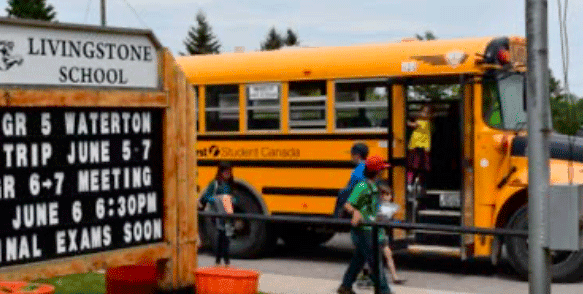 Gelber Schulbus vor dem Schild der Livingstone School – Schulweg im Auslandsjahr in Alberta