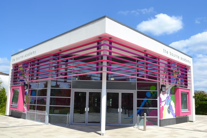 Eingang der Bourne Academy mit pinkfarbener Fassade und buntem Wandbild, Südwestengland
