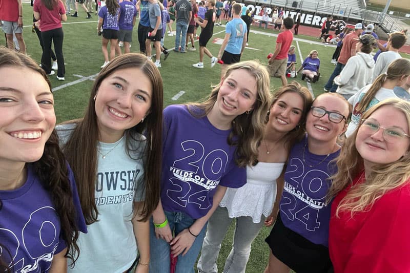Lachende Schülerinnen in lila T-Shirts mit Aufschrift 2024 auf dem Sportfeld einer High School