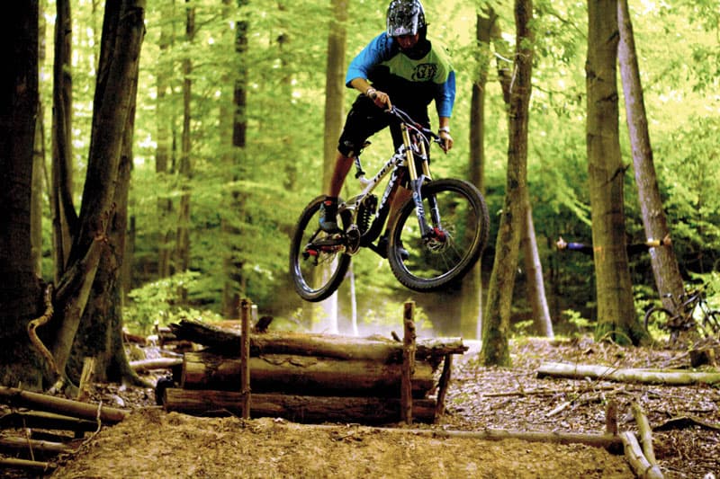 Mountainbiker springt im Wald über einen Holzstamm in Kanada