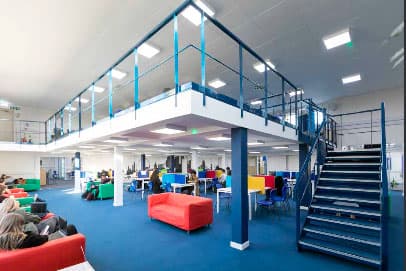 Helle Lernhalle mit Galerie, Treppe und roten Sofas – Schulalltag in England