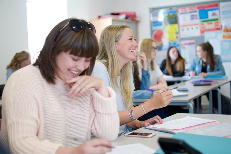Unterricht in Südwestengland: lachende Schülerinnen schreiben an Tischen im Klassenzimmer