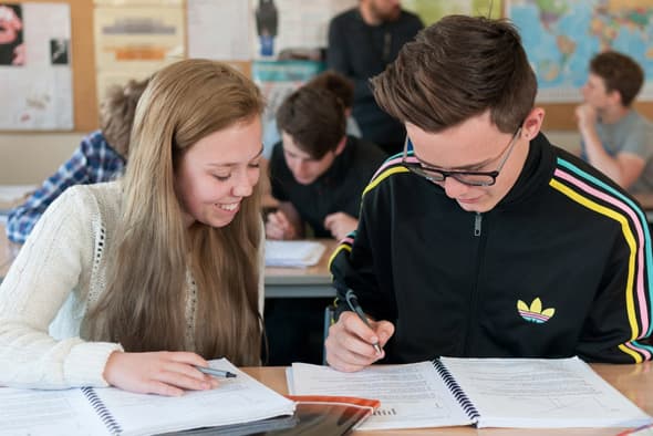 Schülerin und Schüler mit Brille arbeiten gemeinsam in Arbeitsheften im Unterricht in England