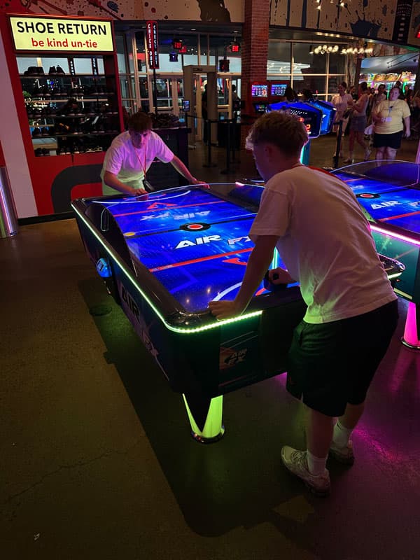 Zwei Austauschschüler:innen spielen Airhockey in einer beleuchteten Spielhalle