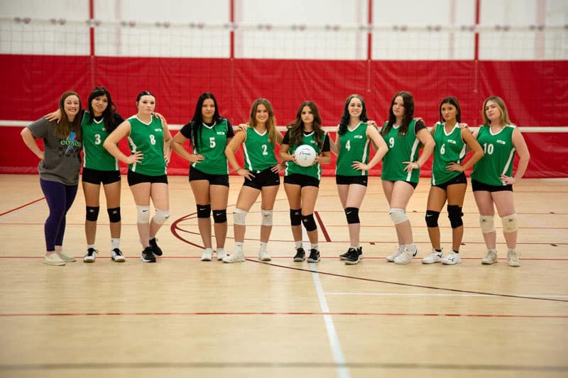 Volleyballteam einer High School in grünen Trikots mit Trainerin in der Sporthalle