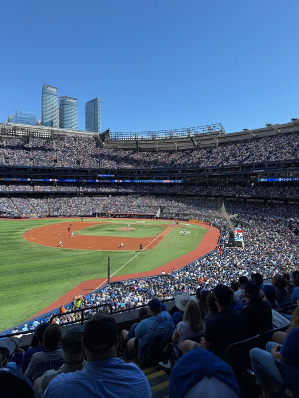 Volles Baseballstadion bei Sonnenschein mit Hochhäusern im Hintergrund, Kanada