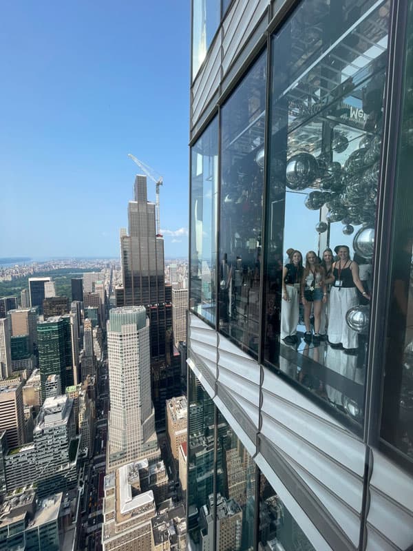 Austauschschüler:innen spiegeln sich in der Glasfassade einer Aussichtsplattform über Manhattan